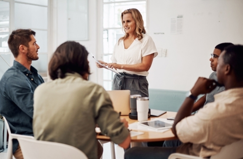 A group of people sitting look up at a woman presenting to them