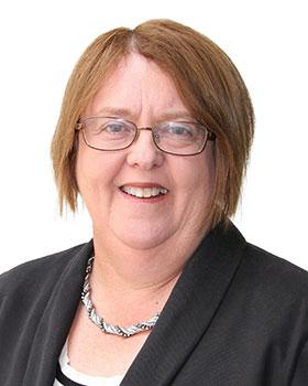 Woman with glasses and dark jacket smiles at camera