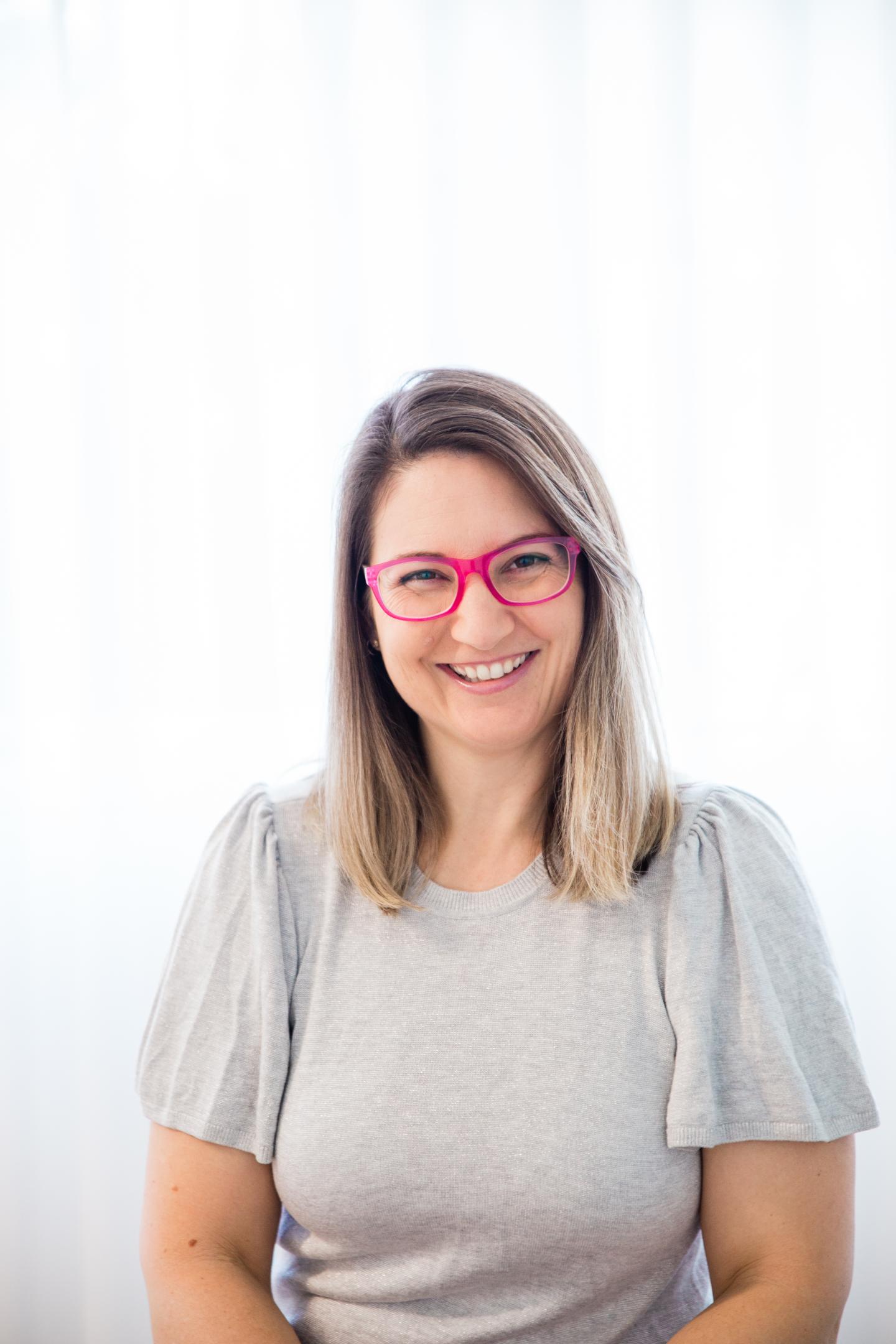 Woman in grey shirt and pink glasses smiling