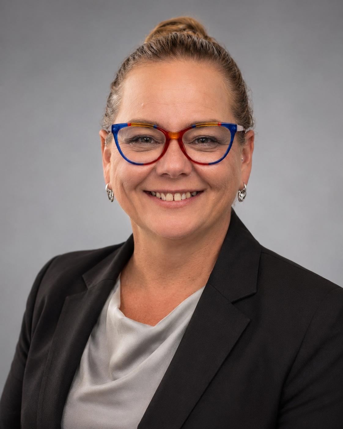 Smiling women in grey shirt, dark jacket and colourful glasses