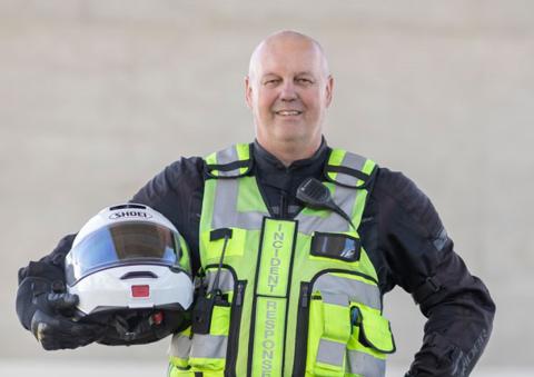 Smiling man in high vis and holding a motorcycle helmet