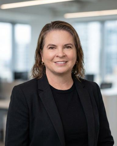 Dark haired woman in an all black suit smiling at the camera.