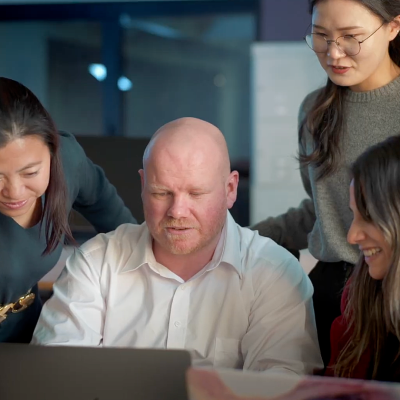 A group of people gather around a laptop